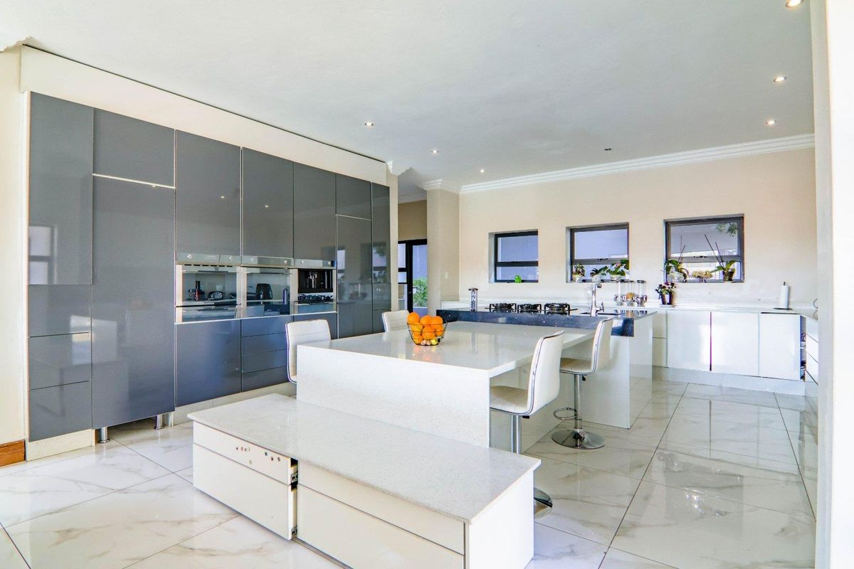 Modern kitchen featuring high-gloss grey cabinetry, a large central island with stone countertops, integrated appliances, and polished porcelain tile flooring.