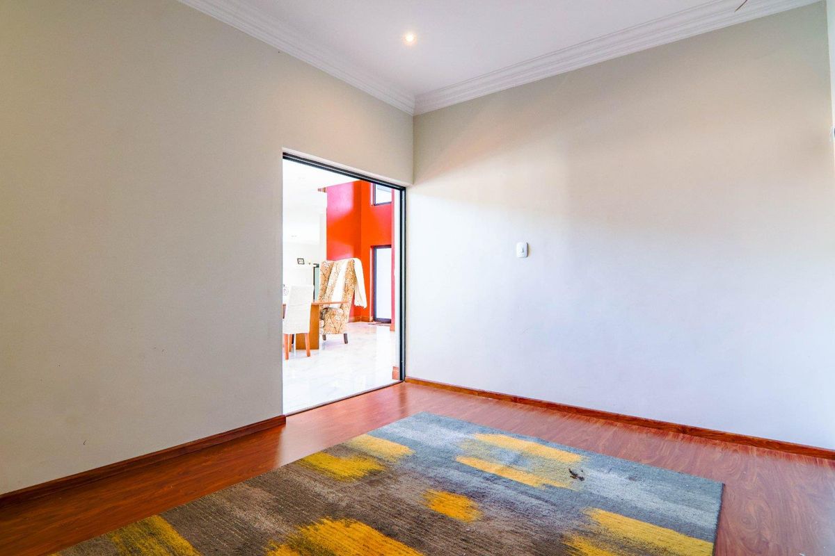 A bright, empty living room featuring laminate flooring, recessed downlighting, and decorative cove cornicing, with a clear view into the adjacent living space.