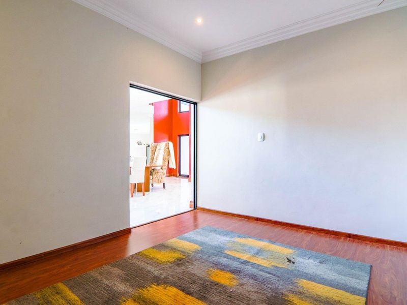 A bright, empty living room featuring laminate flooring, recessed downlighting, and decorative cove cornicing, with a clear view into the adjacent living space.