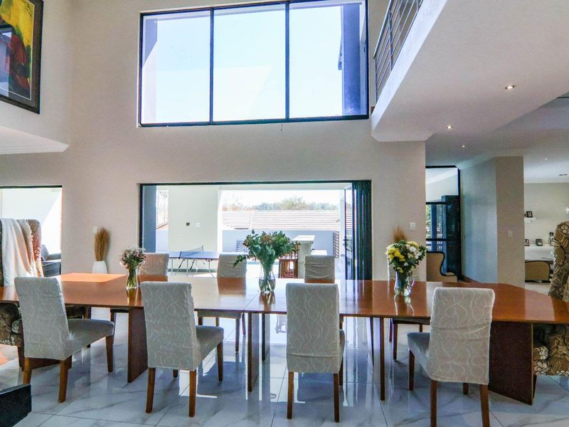 Spacious double-volume dining area featuring large windows, polished tiled floors, and seamless access to the outdoor patio through stacking doors.