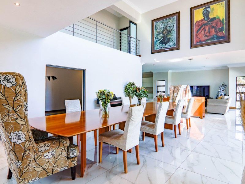 Spacious open-plan living and dining area featuring double-volume ceilings, polished marble-look floor tiles, and a mezzanine level with a modern stainless steel balustrade.