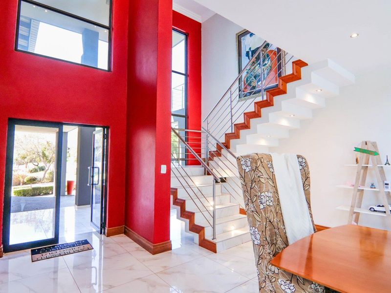 Spacious double-volume entrance hall featuring a modern staircase with stainless steel balustrades, large windows, and polished tiled flooring.