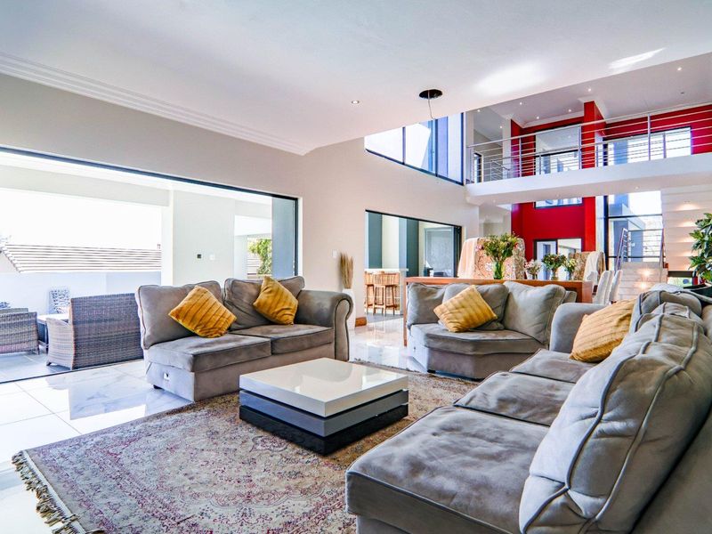Spacious open-plan living area featuring double volume ceilings, a mezzanine level with stainless steel balustrades, and large stacking doors leading to the patio.