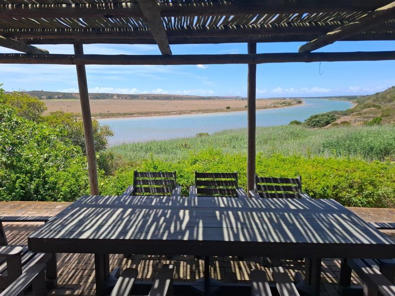 Covered outdoor patio area featuring a rustic timber pergola structure, offering expansive views over the river and natural landscape.