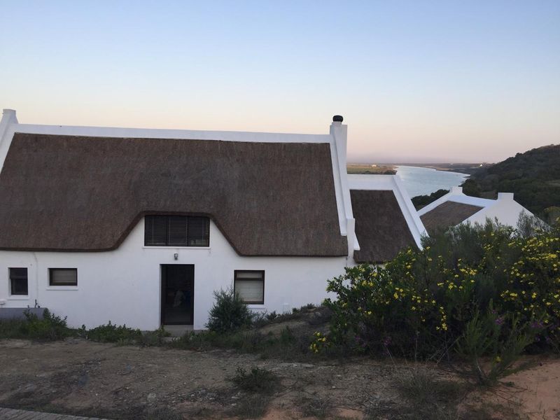 A charming farmhouse with a traditional thatched roof, featuring white exterior walls and scenic views of the nearby river and landscape.