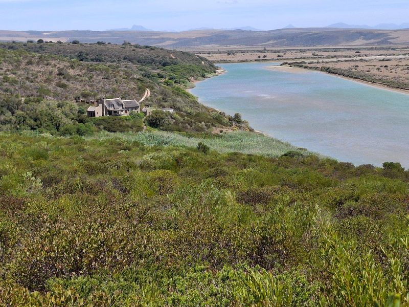 An elevated landscape view showcasing the farm property situated along the riverbank, surrounded by natural vegetation and scenic hills.