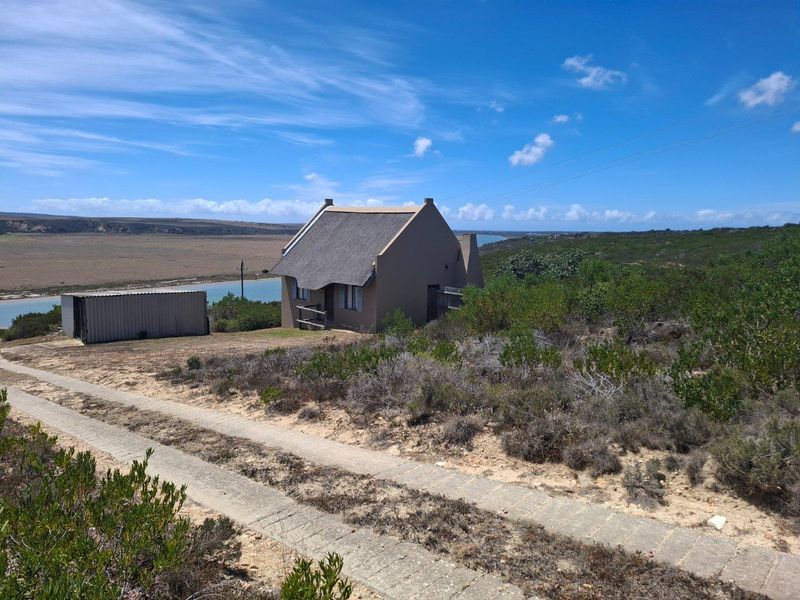 A charming thatched-roof cottage situated on a rural farm property, featuring a scenic landscape view and a concrete driveway approach.