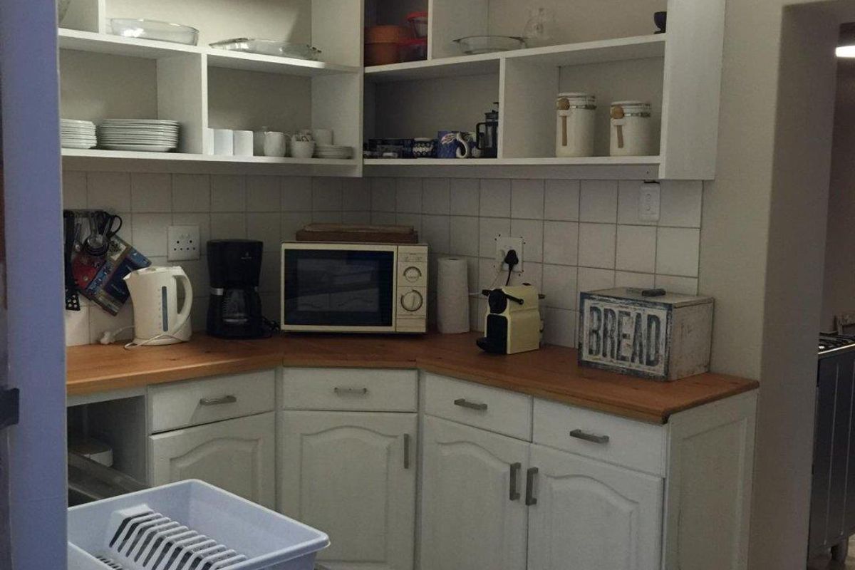 A functional kitchen area featuring white cabinetry, wooden countertops, tiled backsplash, and open shelving under a rustic thatched roof structure.