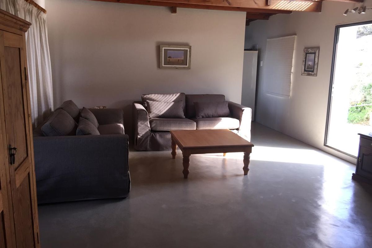 A living room featuring exposed timber ceiling beams and polished concrete flooring, with large sliding glass doors providing natural light and garden access.