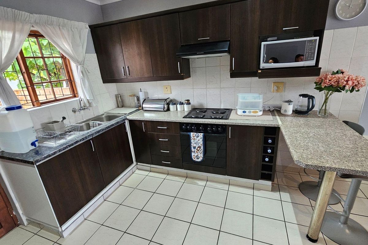 A functional kitchen featuring dark wood-look cabinetry, granite-style countertops, a built-in oven with hob, extractor fan, and a breakfast bar area.
