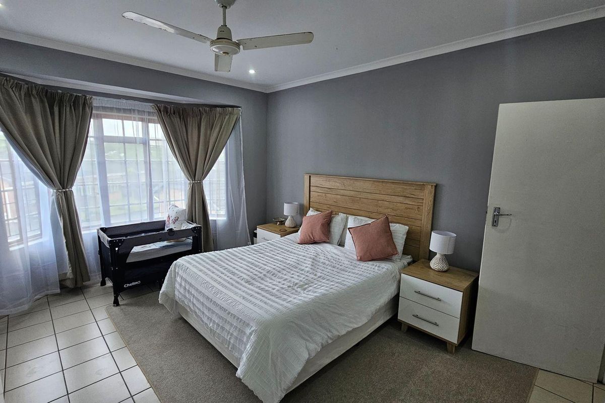 A well-maintained bedroom featuring tiled flooring, a ceiling fan, and large windows that provide ample natural light.