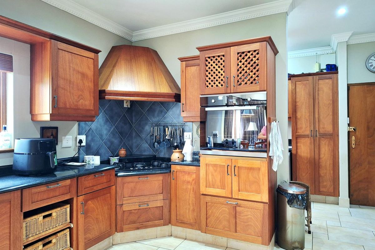A traditional kitchen featuring warm-toned wooden cabinetry, a built-in oven, a gas hob with an extractor hood, and tiled flooring.