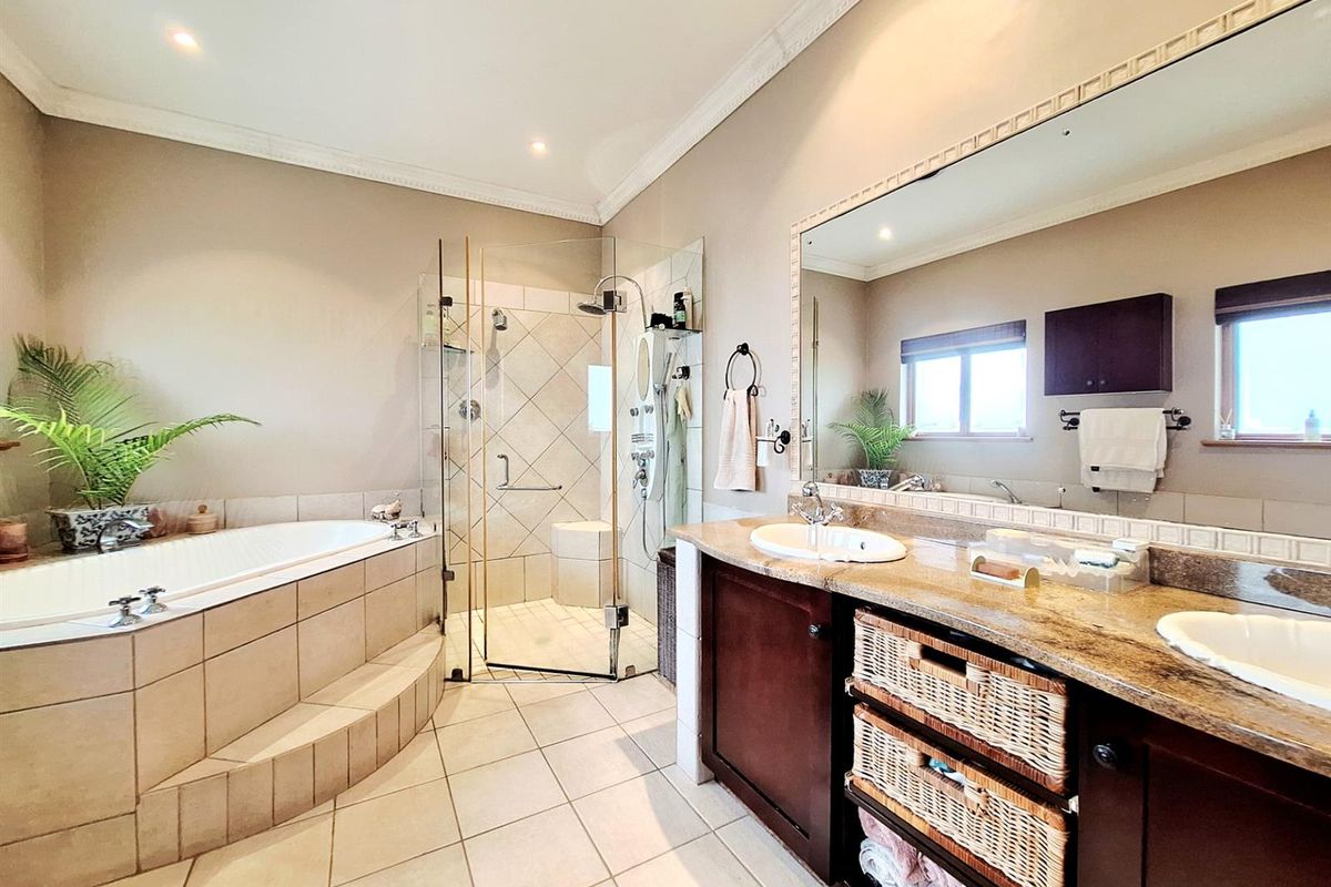 Spacious bathroom featuring a built-in soaking tub, a glass-enclosed shower, and a double vanity with granite countertops and ample storage.
