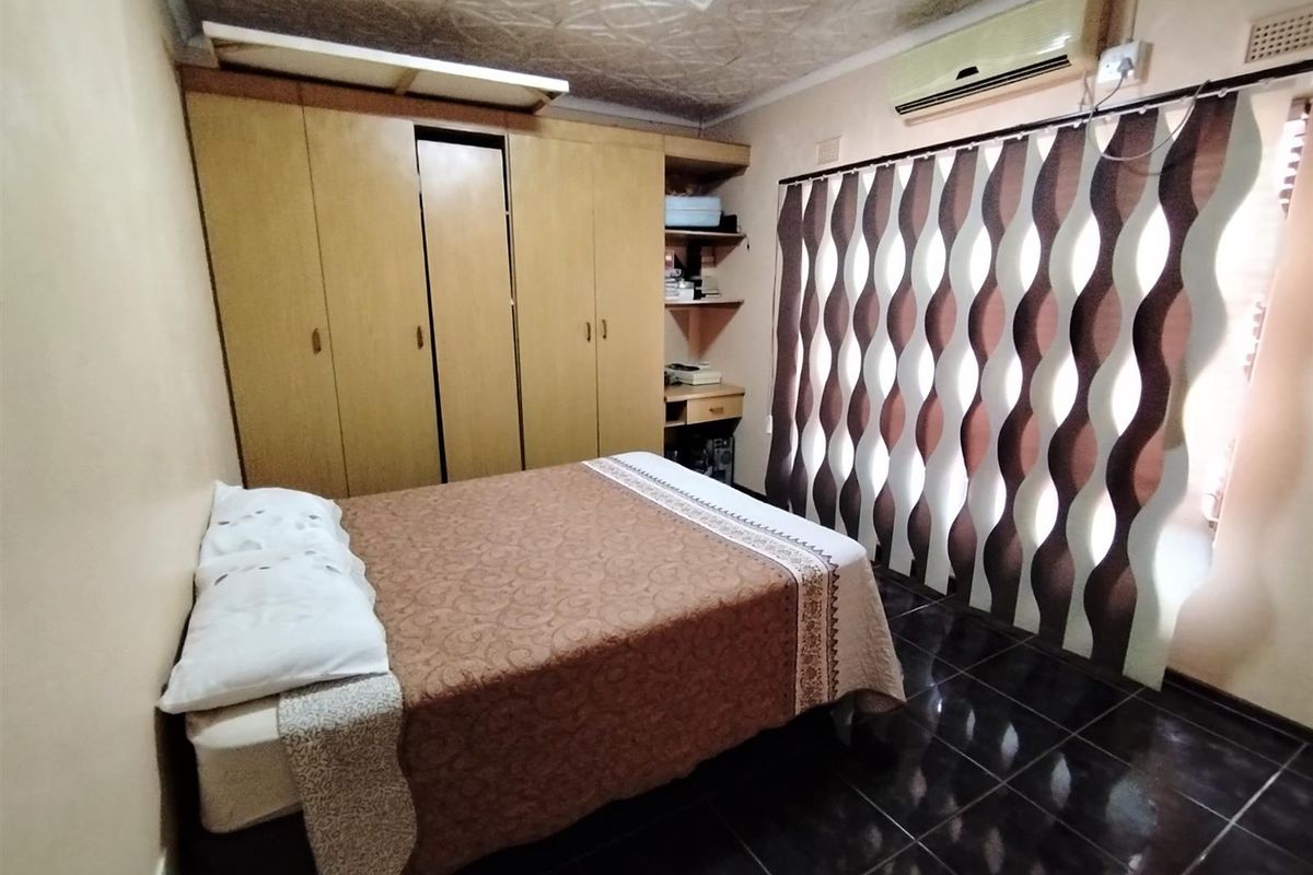 A bedroom featuring built-in wooden cabinetry, dark floor tiles, and a wall-mounted air conditioning unit.