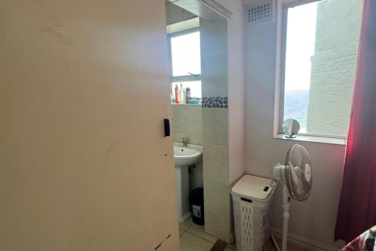 A view into a small bathroom featuring a pedestal sink and tiled flooring, accessed via a sliding door.