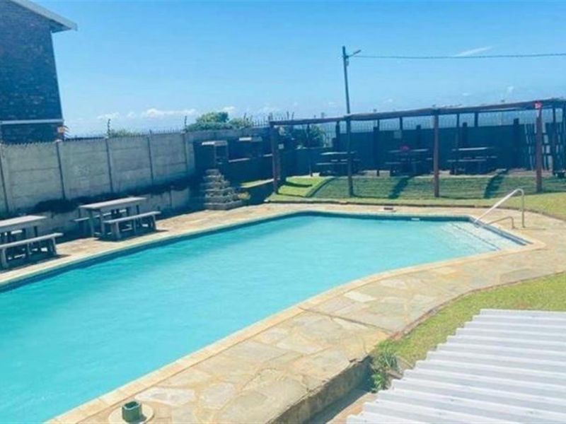 Communal outdoor pool area featuring a swimming pool, paved surround, lawn, and a covered pergola structure for outdoor seating.