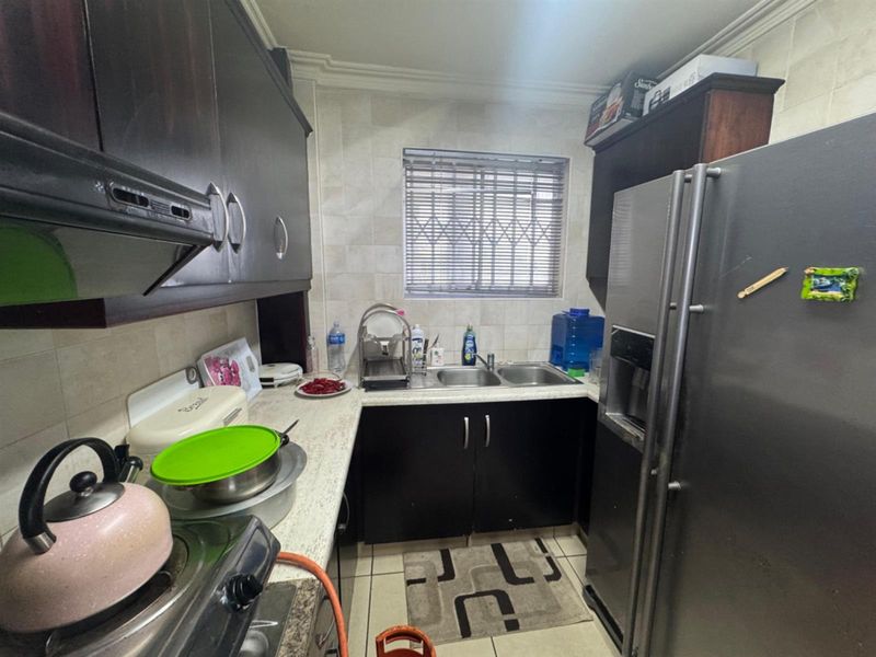 Compact kitchen featuring dark cabinetry, double basin sink, tiled backsplash, and window with security bars.