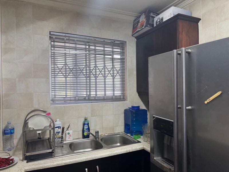 A functional kitchen area featuring a double stainless steel sink, tiled backsplash, and dark cabinetry with a window providing natural light.