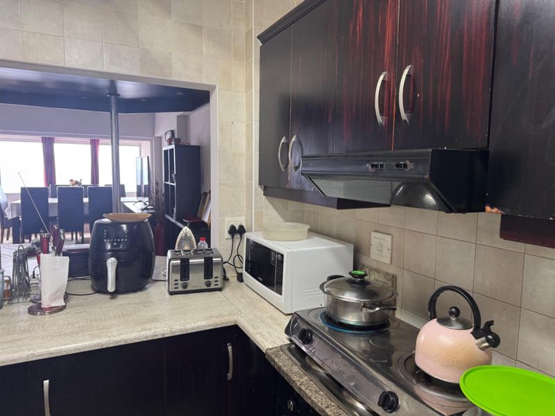A functional kitchen featuring dark wood-finish cabinetry, a built-in extractor fan, and a tiled backsplash, with an open-plan layout connecting to the dining area.