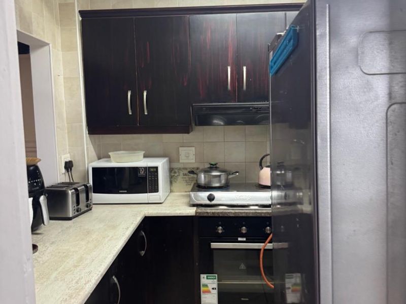 Compact kitchen featuring dark cabinetry, light-toned countertops, built-in oven, and hob with an extractor fan.