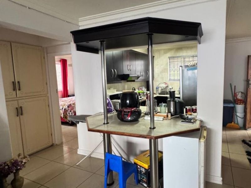 Open plan kitchen area featuring a breakfast bar with metal supports, tiled flooring, and built-in cabinetry with a pass-through window to the kitchen.