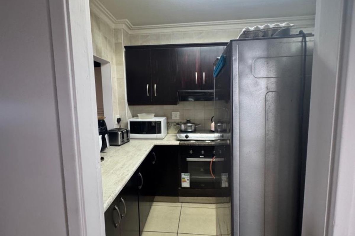 A compact kitchen featuring dark cabinetry, light-toned countertops, tiled flooring, and built-in cooking appliances, viewed from the doorway.