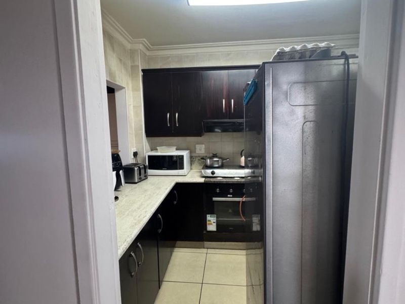 A compact kitchen featuring dark cabinetry, light-toned countertops, tiled flooring, and built-in cooking appliances, viewed from the doorway.
