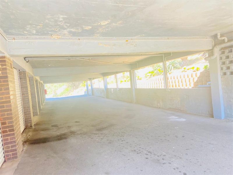 A covered parking area featuring concrete flooring, brick support pillars, and exposed ceiling structure.
