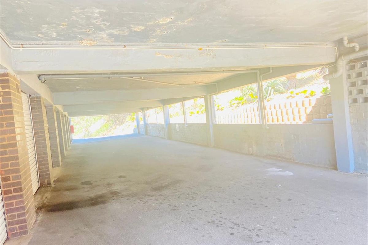 A covered parking area featuring concrete flooring, brick support pillars, and exposed ceiling structure.