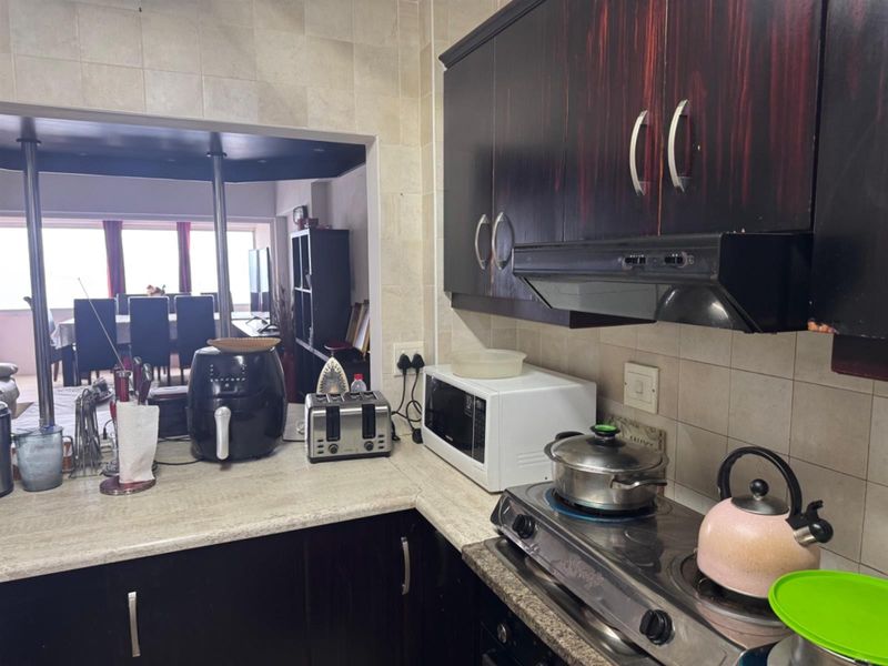 A functional kitchen featuring dark built-in cabinetry, a gas hob with extractor fan, and tiled backsplash, opening into the adjacent living area.