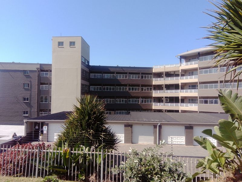 Exterior view of a multi-story apartment complex featuring a row of ground-level garages and a secure perimeter fence.