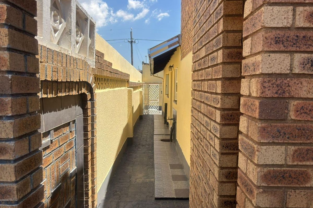 A narrow side passage featuring brick walls, a tiled walkway, and an external water tap leading to a rear security gate.