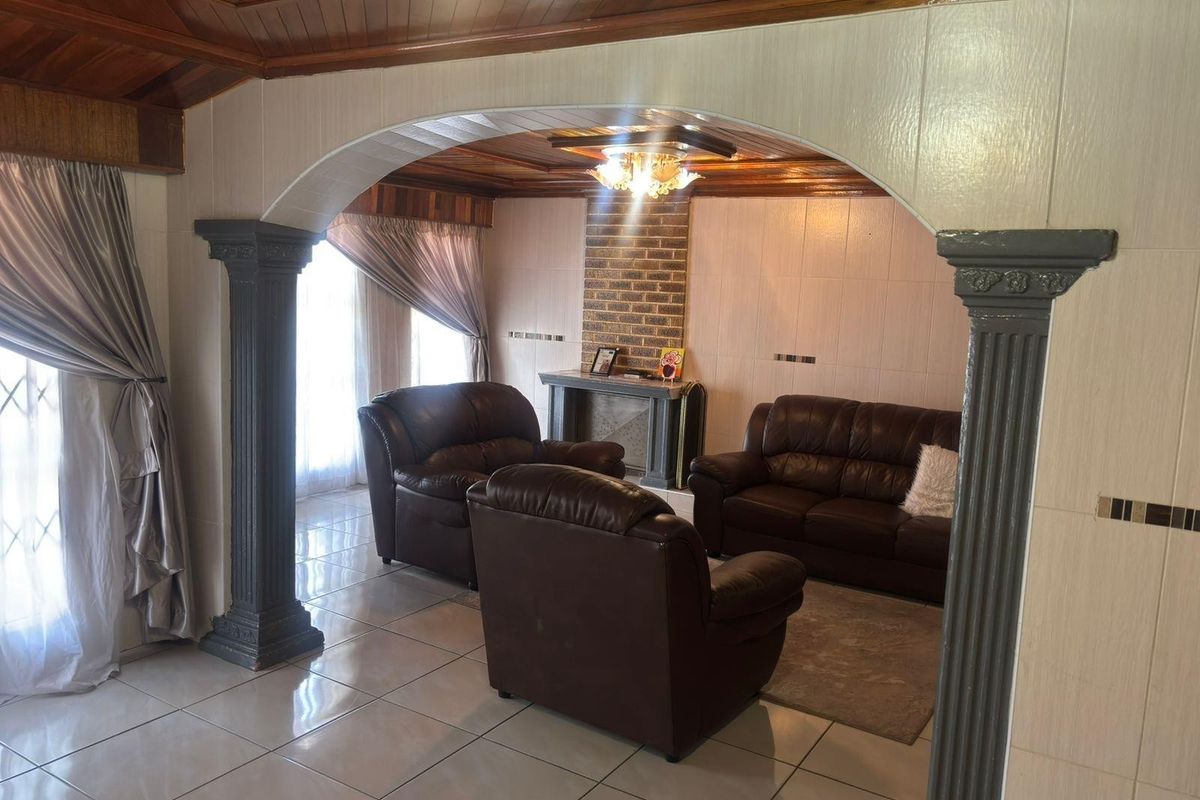 Spacious living room featuring a distinctive arched entryway with decorative columns, a brick fireplace, and warm timber ceiling finishes.