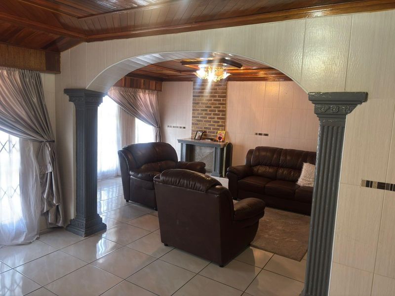 Spacious living room featuring a distinctive arched entryway with decorative columns, a brick fireplace, and warm timber ceiling finishes.