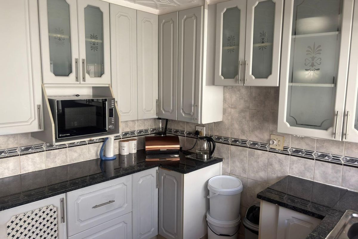 A functional kitchen featuring granite countertops, ample built-in cabinetry with glass-fronted upper units, and a decorative tiled backsplash.