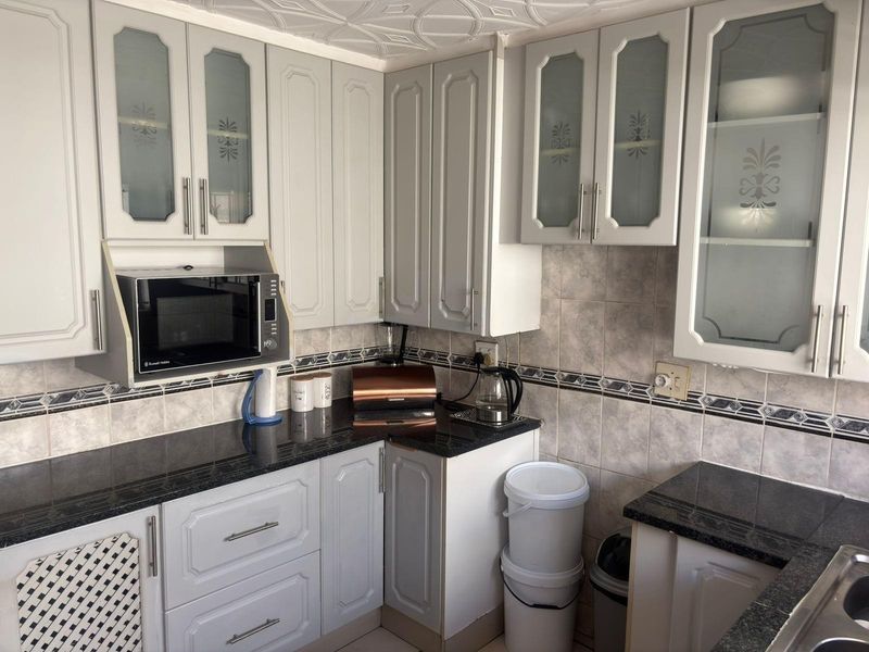 A functional kitchen featuring granite countertops, ample built-in cabinetry with glass-fronted upper units, and a decorative tiled backsplash.
