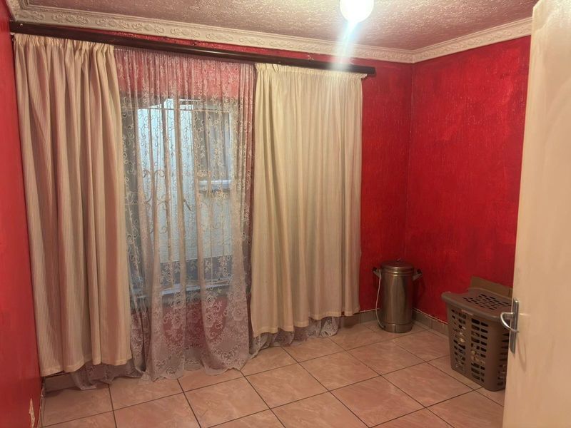 A vacant bedroom featuring tiled flooring, decorative ceiling cornices, and security bars on the window, ready for a modern update.