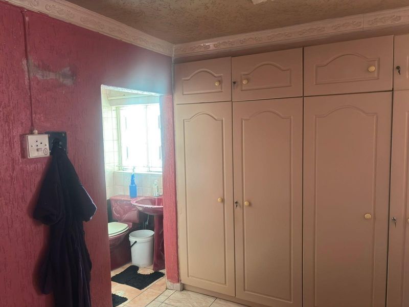 Bedroom featuring built-in cupboards and textured walls, with an adjoining en-suite bathroom visible through the doorway.