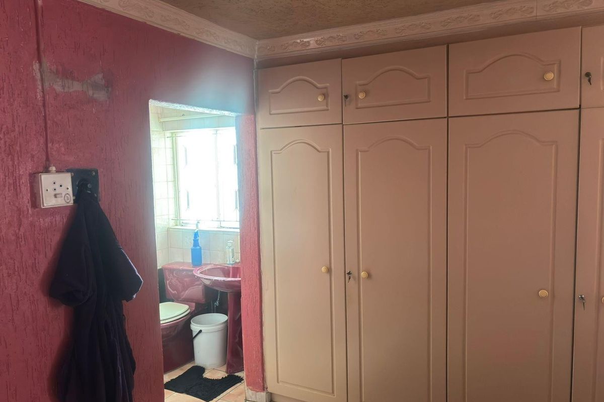 Bedroom featuring built-in cupboards and textured walls, with an adjoining en-suite bathroom visible through the doorway.