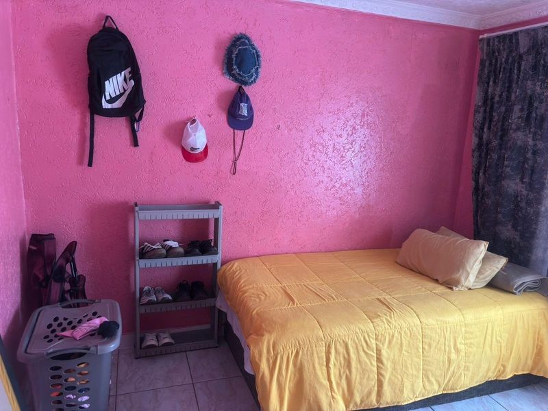 A bedroom featuring tiled flooring, textured pink walls, and decorative ceiling cornicing, offering a functional space ready for cosmetic updates.