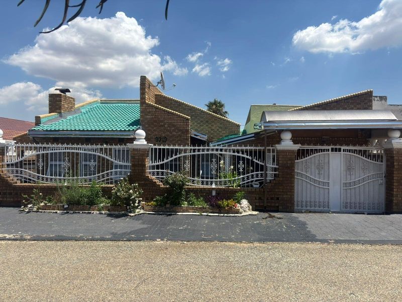 Front elevation of a face-brick house featuring a secure wrought iron perimeter fence, gated driveway, and a covered carport area.