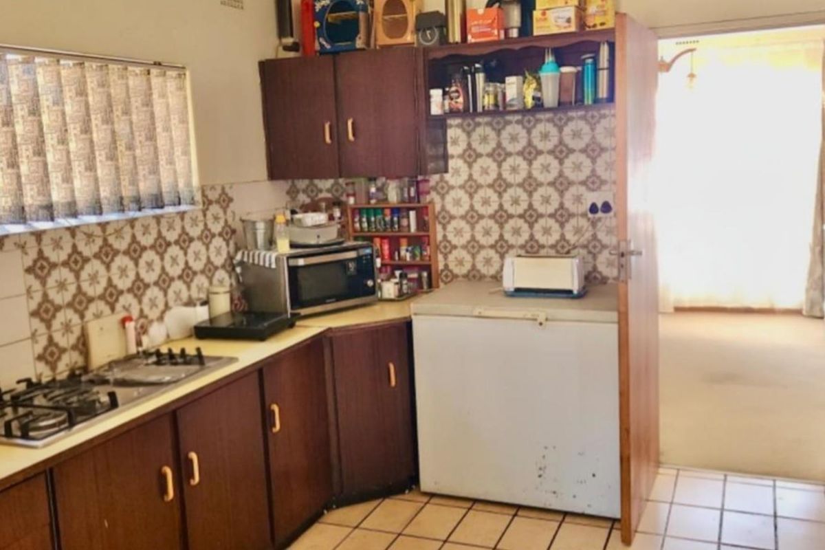 A dated kitchen featuring dark wood cabinetry, patterned wall tiles, and tiled flooring, offering a functional layout with built-in gas hob.