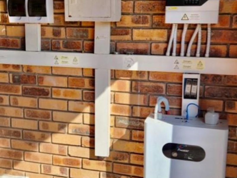 A wall-mounted solar inverter and battery storage system installed on an exposed brick wall, featuring integrated electrical conduits and distribution boards.