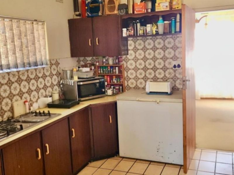 A dated kitchen featuring dark wood cabinetry, patterned wall tiles, and tiled flooring, offering a functional layout with built-in gas hob.