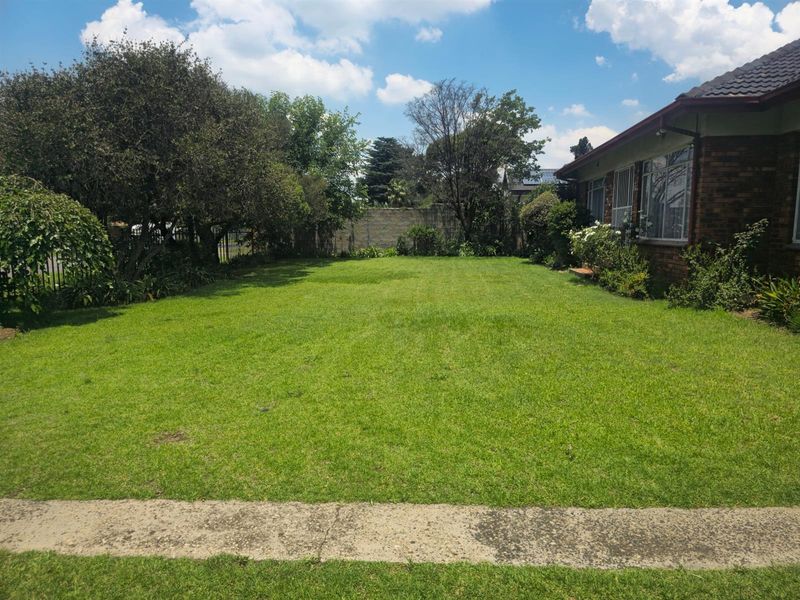 A spacious, well-maintained rear garden featuring a large lawn area, mature trees, and a brick exterior wall of the house.