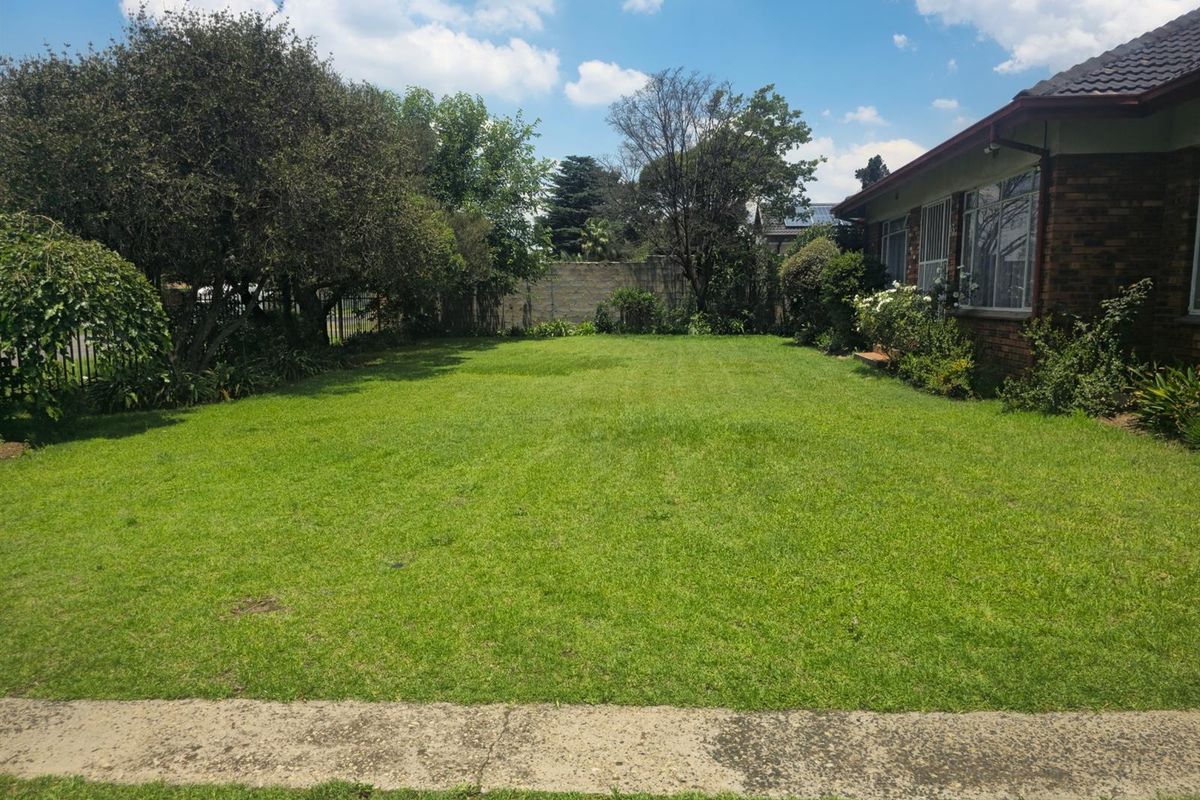 A spacious, well-maintained rear garden featuring a large lawn area, mature trees, and a brick exterior wall of the house.