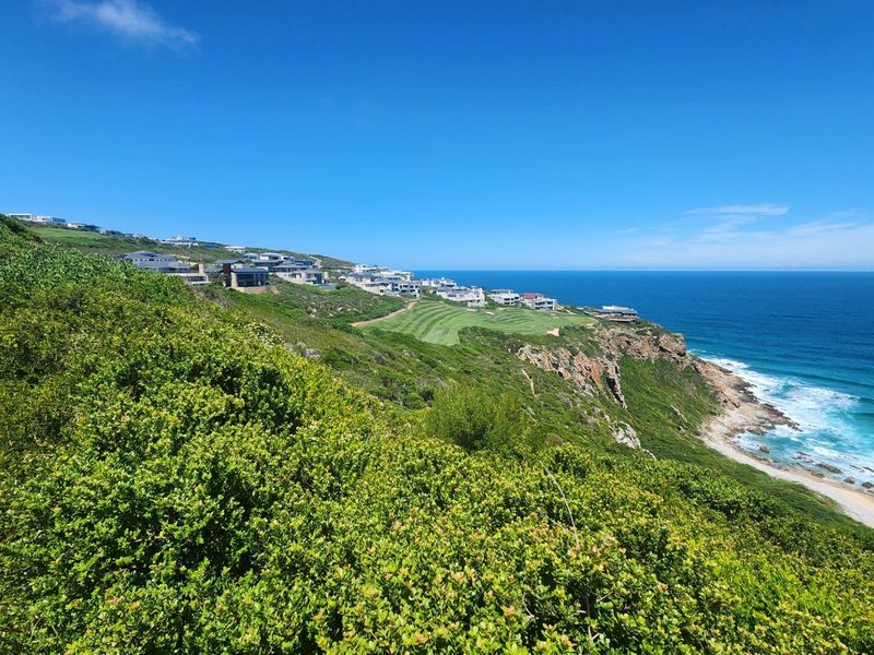 A scenic coastal view overlooking the ocean, rugged cliffs, and a nearby residential estate with manicured green spaces.