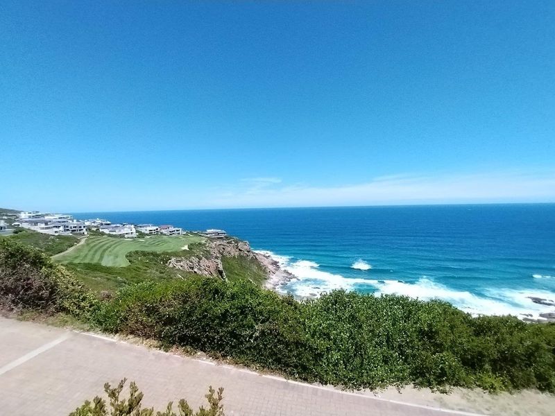 A scenic coastal view overlooking the ocean, rugged cliffs, and a nearby golf course estate.