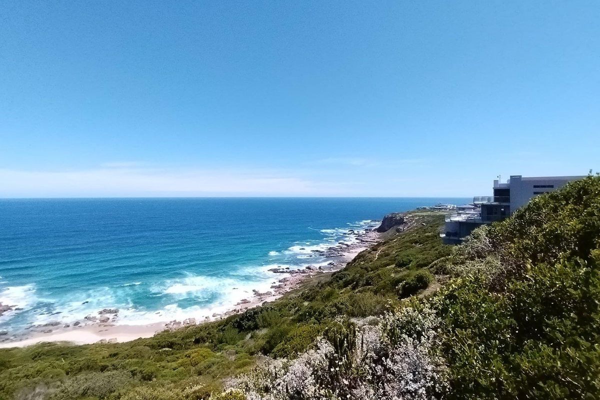 A scenic coastal view overlooking the ocean, rocky shoreline, and natural vegetation, showcasing the prime location of the vacant land.