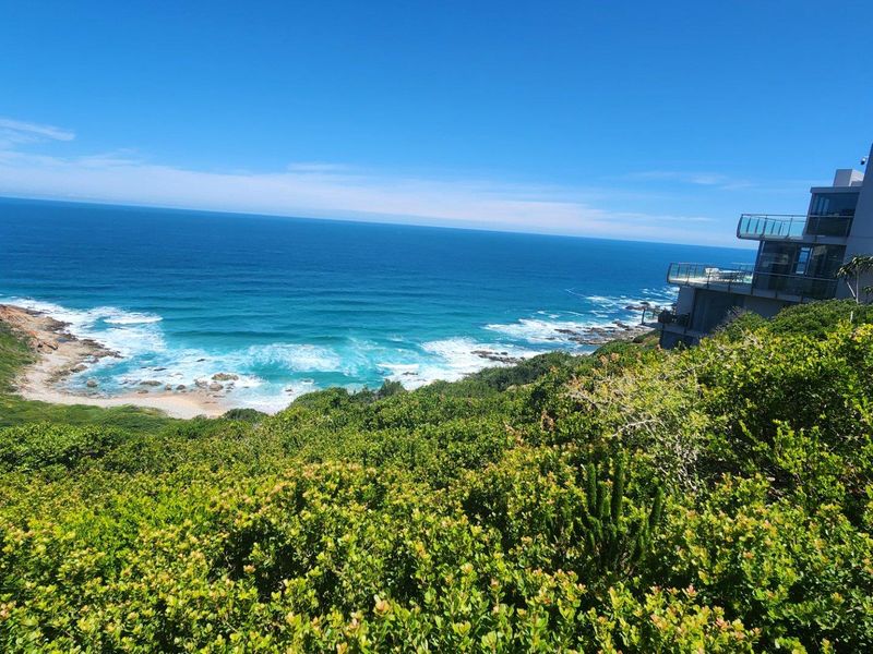 A scenic elevated view overlooking the coastline, featuring lush coastal vegetation and a modern multi-level residential property in the distance.